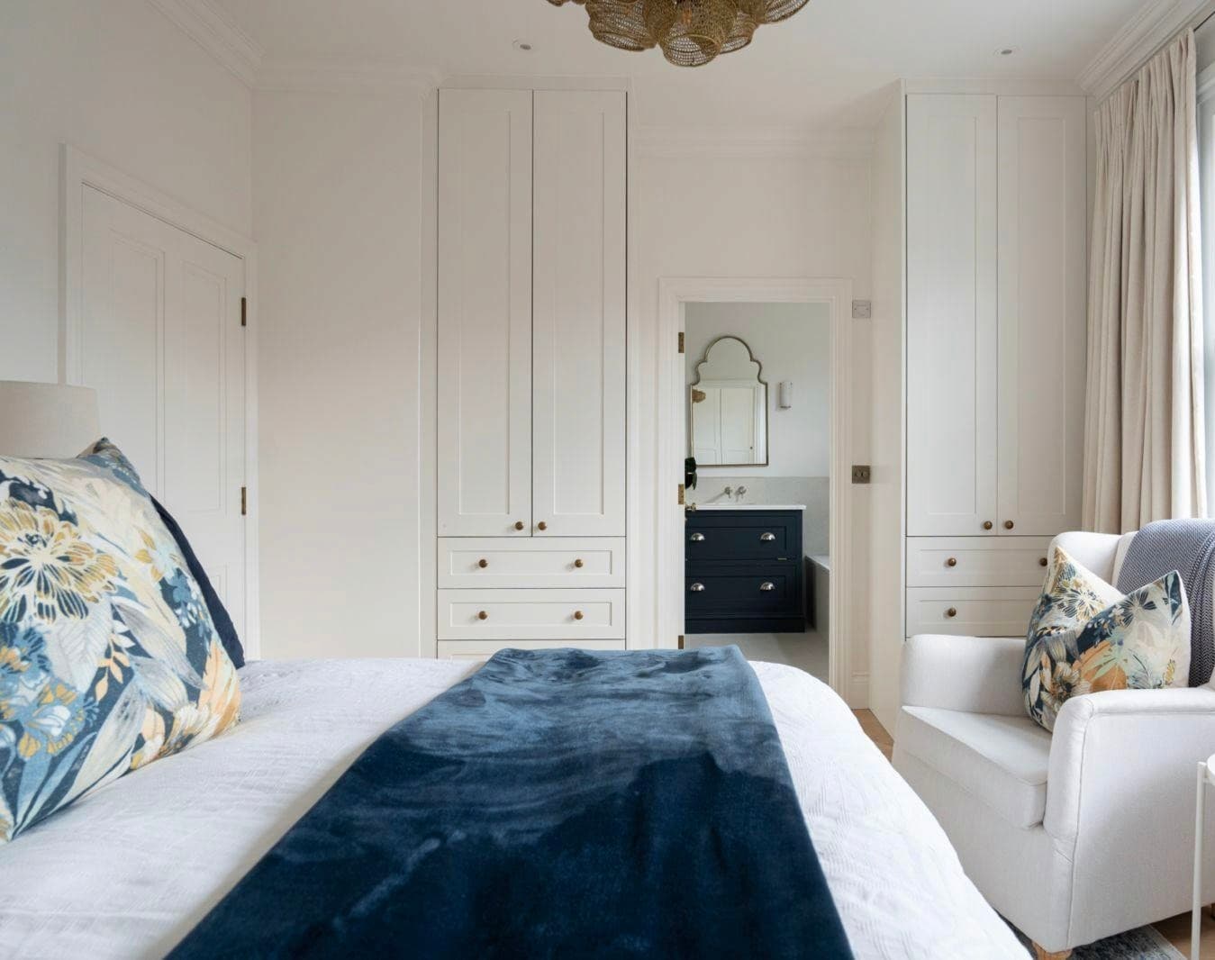Bedroom with floor-to-ceiling fitted wardrobes, a navy velvet throw and botanical cushions — Roehampton, London